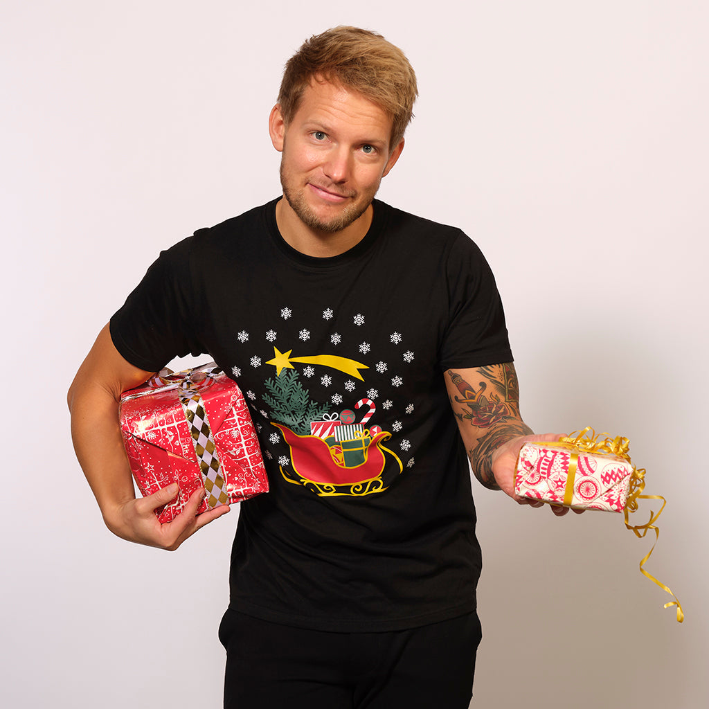 En mand med gaver i hænderne står iklædt en sort T-shirt med juletema.